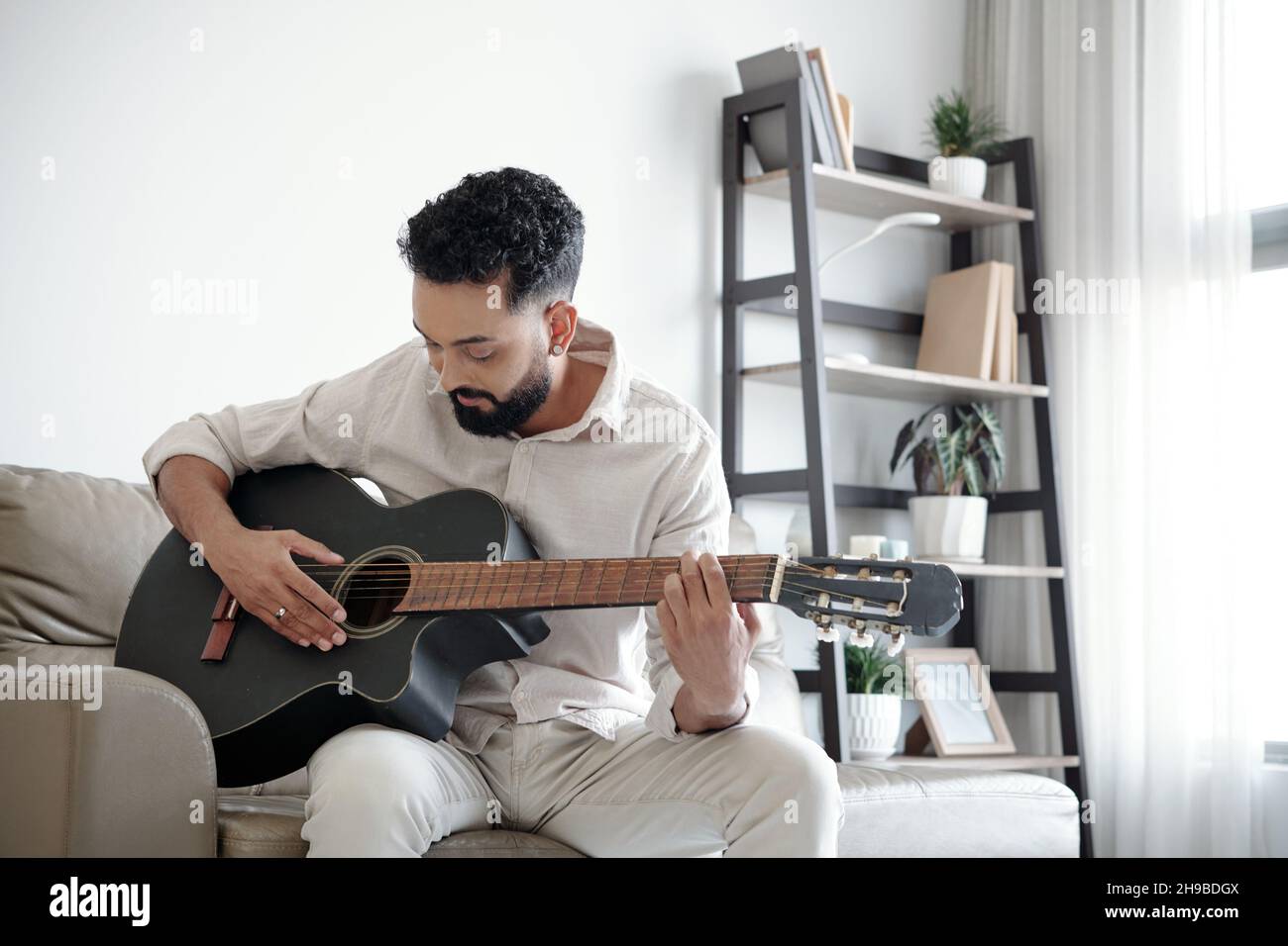 Handsome man sitting on sofa at home and playing guitar Stock Photo
