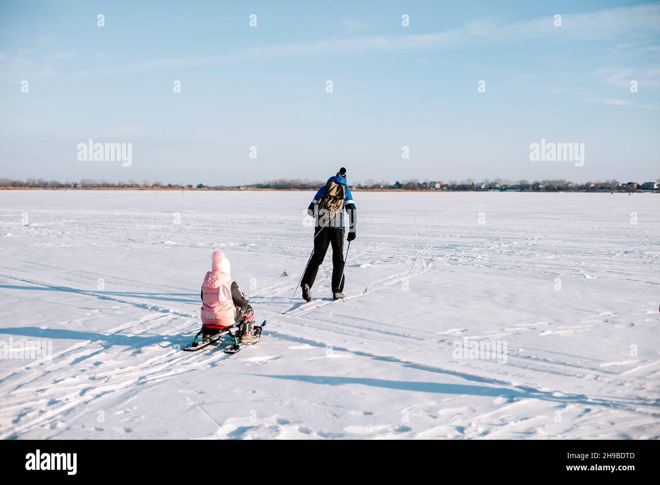 Family on winter walk. Young man and child are skiing in winter on frozen river near forest, man is sledding child in snow Stock Photo