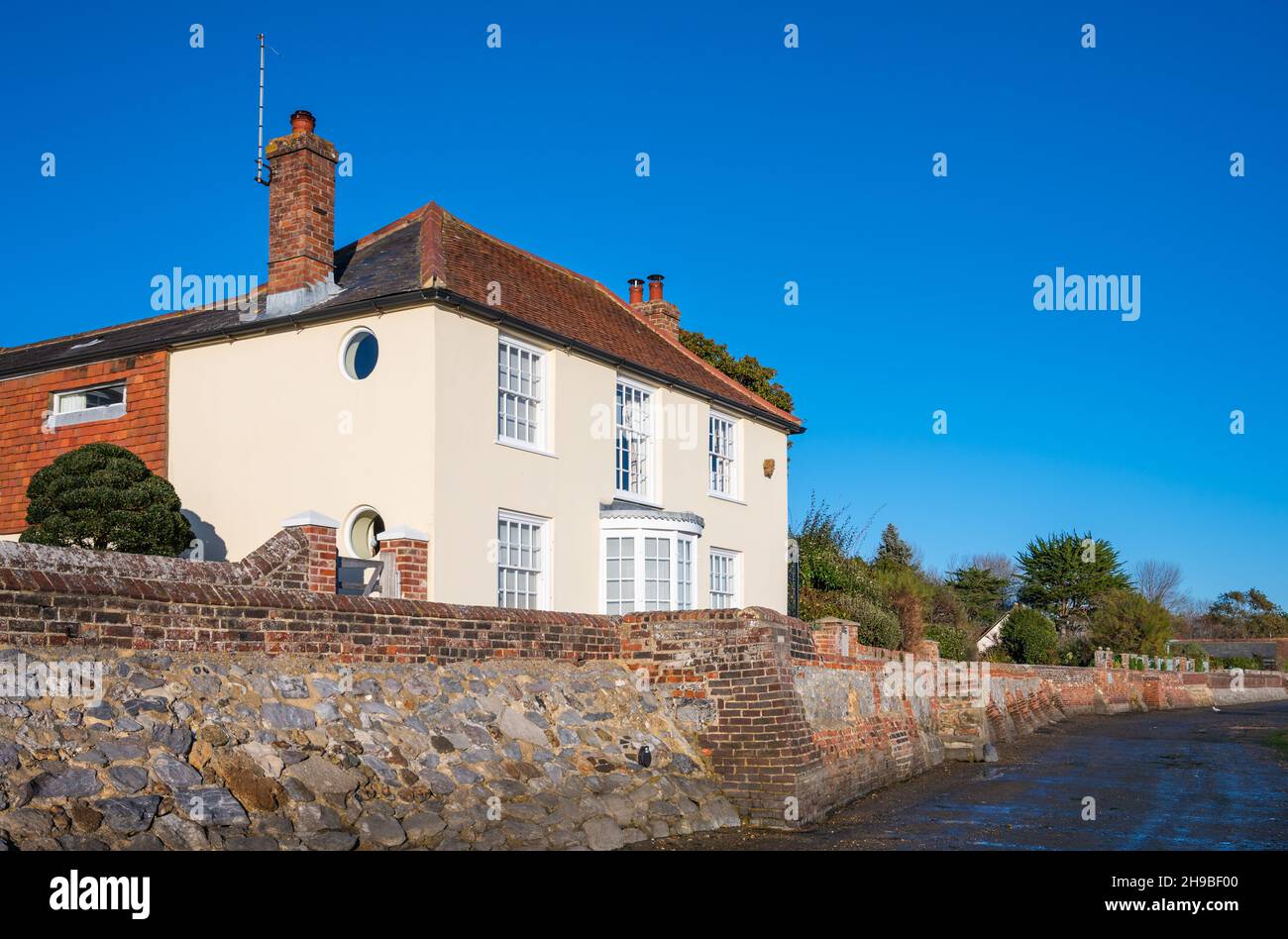 Mariner's Cottage, a Grade II Listed 18th century waterfront home behind boundary wall made from Mixen Stone on Shore Road in Bosham Village, UK. Stock Photo