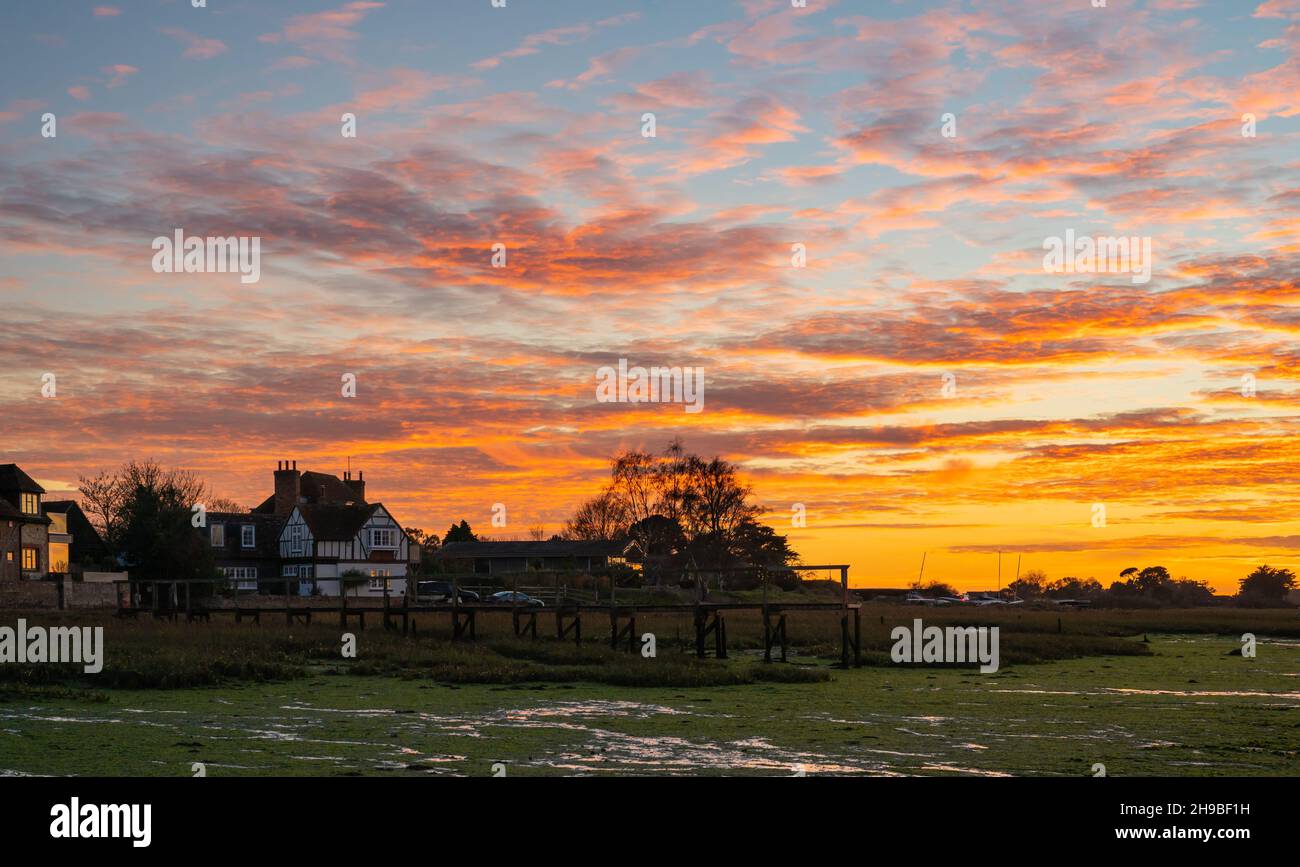 Beautiful cloudy orange sky after sunset over Bosham Quay (Bosham Creek) at Chichester Harbour at low tide in Winter in West Sussex, England, UK. Stock Photo