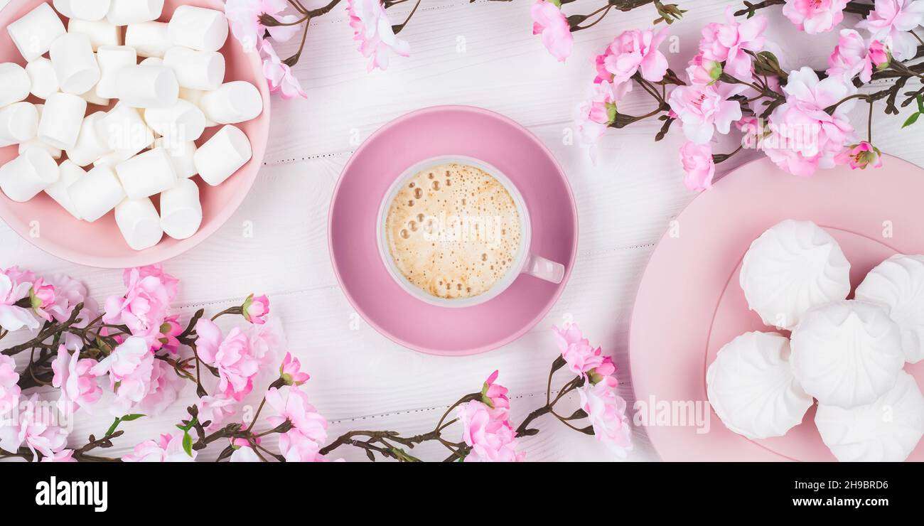Romantic spring still life. Coffee cup with marshmallow in the morning for breakfast. Cherry blossom on white wooden background. Flat lay. Pastel pink Stock Photo