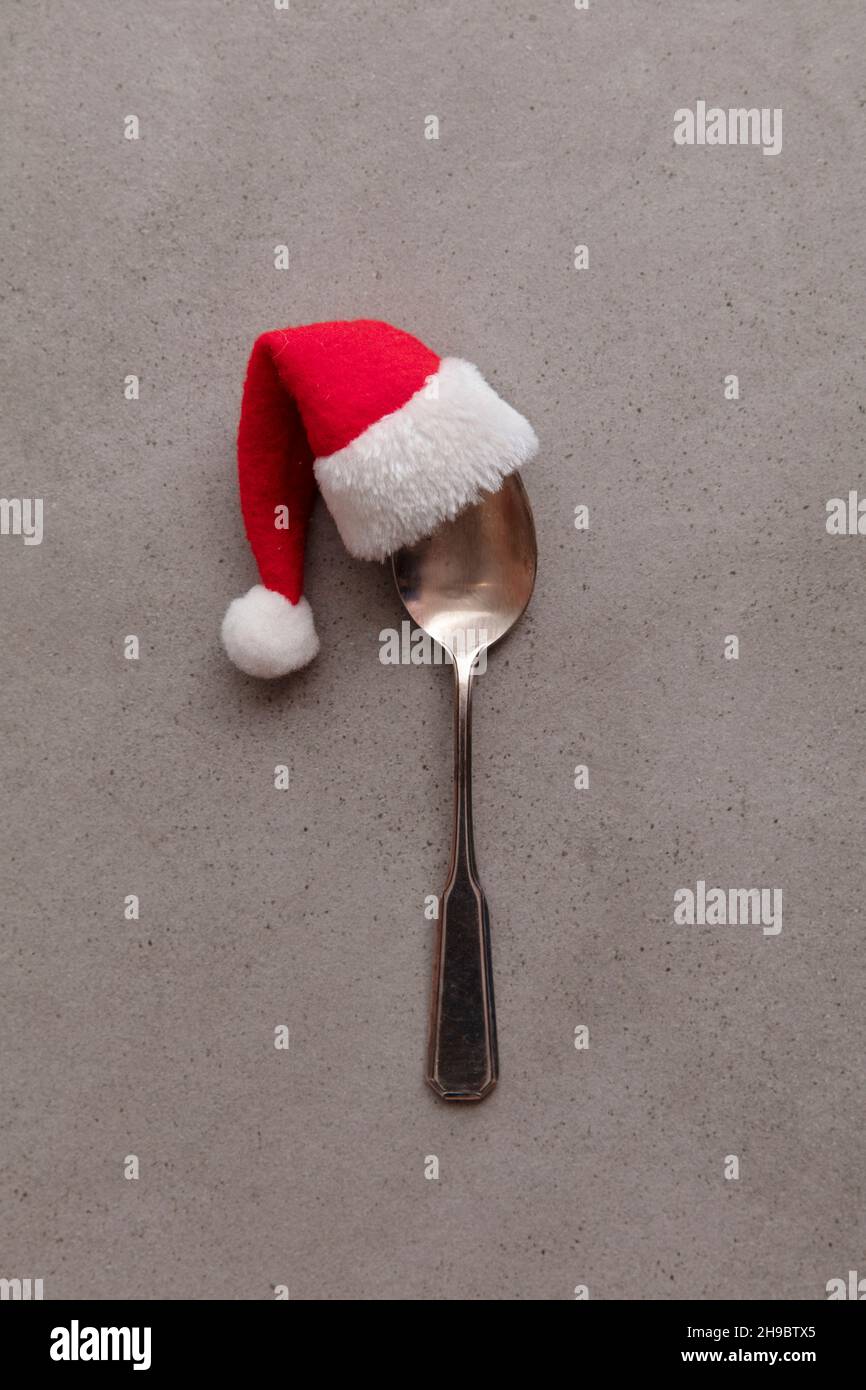 Silver spoon wearing a red Santa hat. Christmas meal background Stock Photo