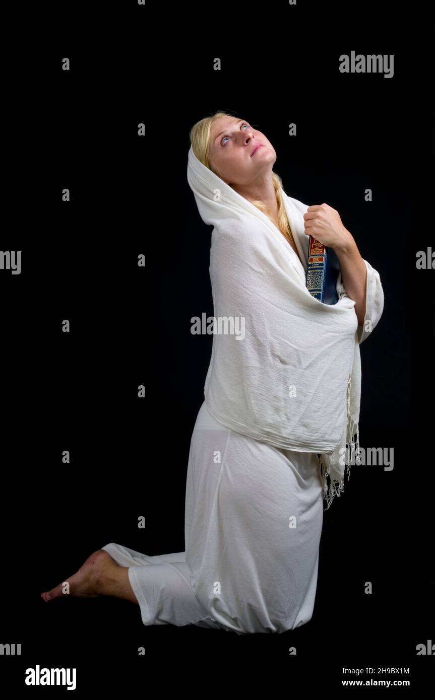 Young woman on her knees in an intimate moment of faith on black background Stock Photo