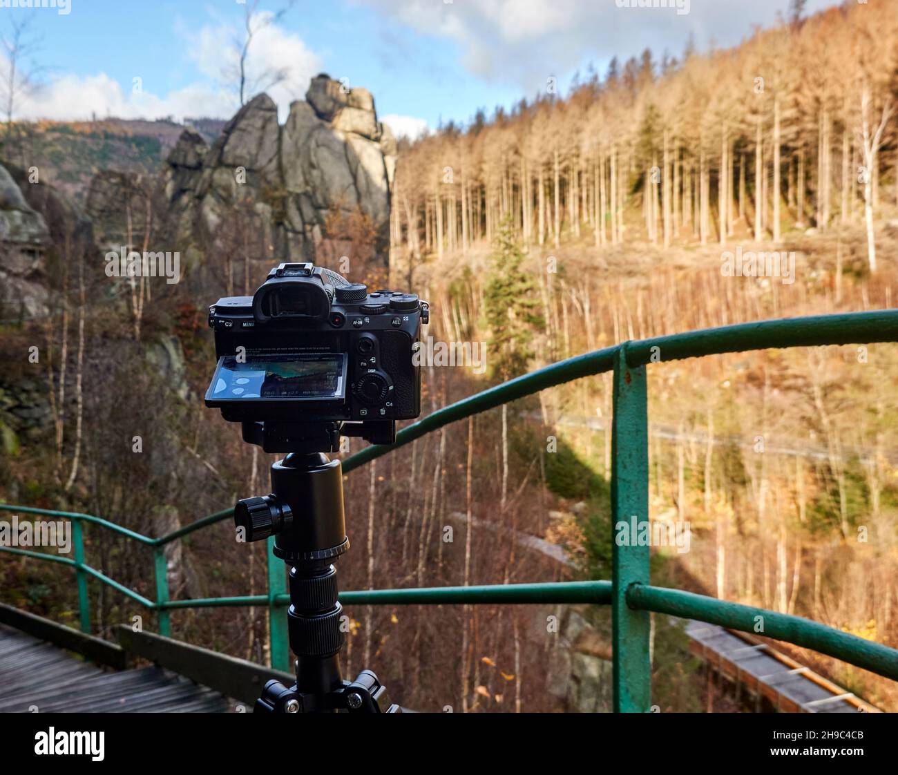 Camera on a tripod films a rock scenery behind a green railing Stock Photo