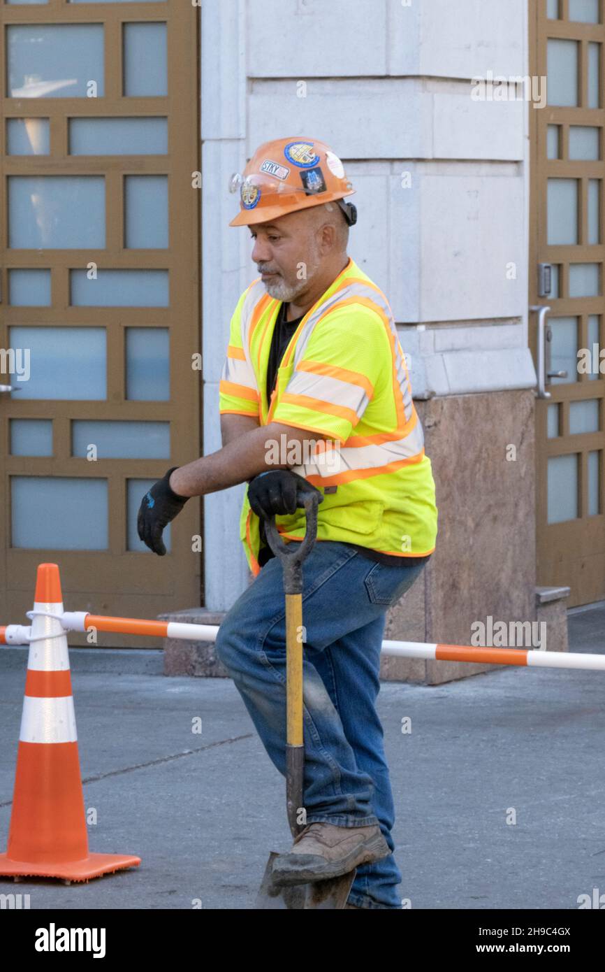 A construction worker in a helmet and safety vest takes a brief break. In Williamsburg, Brooklyn, New York City. Stock Photo