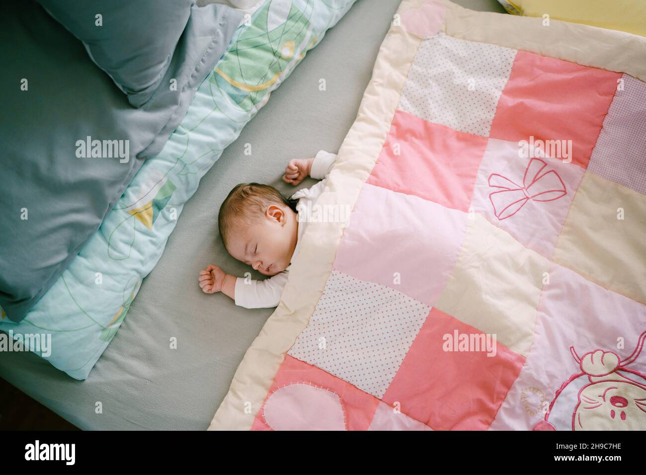 Infant sleeps on bed covered with pink patchwork quilt. Top view Stock
