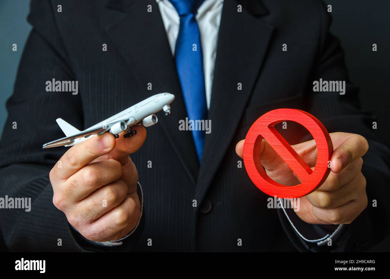 Man is holding an airplane and a red NO sign. Ban on flights. Non-flying zone. Lack of air transporting capacity. Embargo, sanctions. Transport crisis Stock Photo