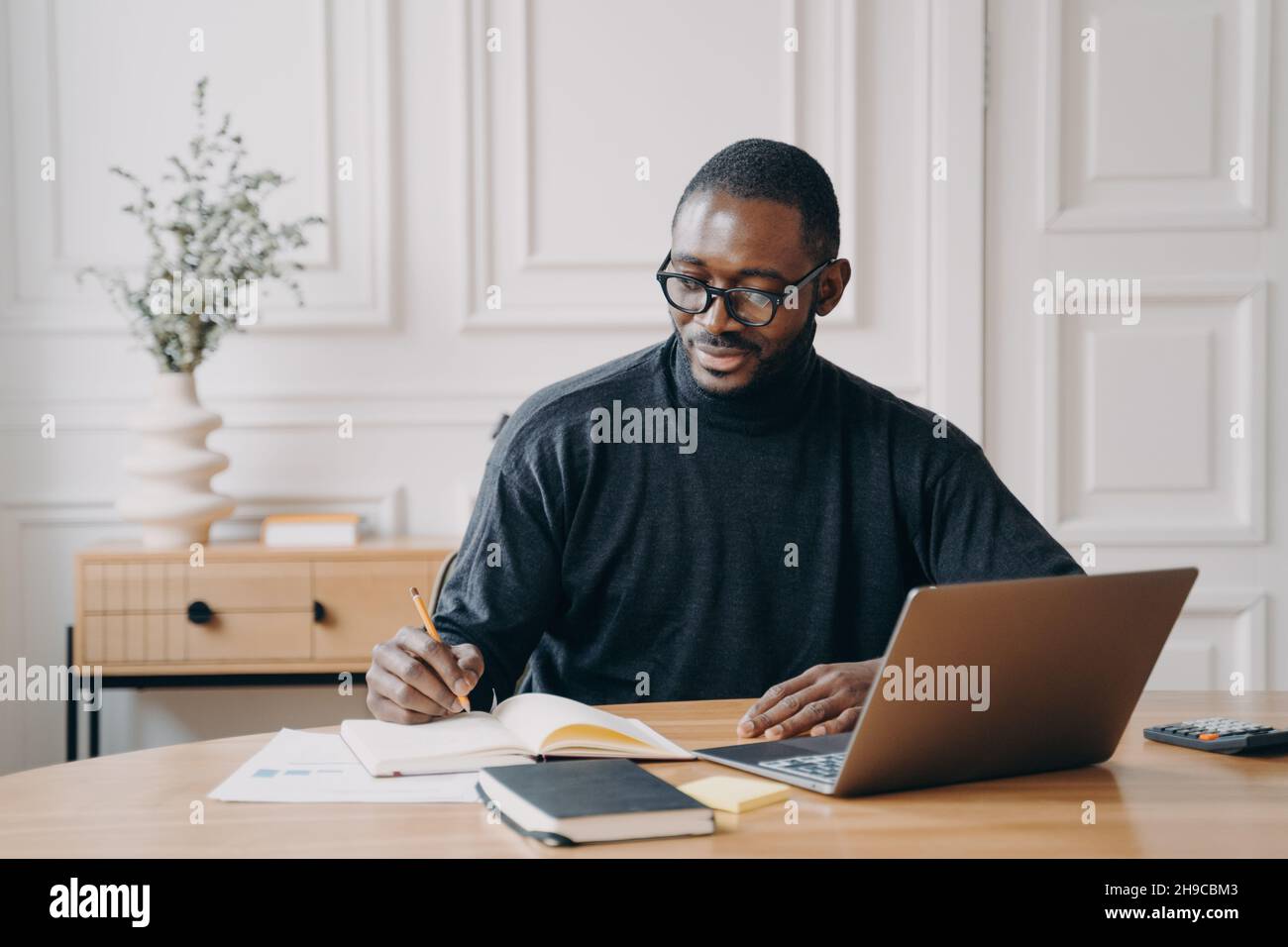 Focused young african american businessman writing down notes in notebook while working in office Stock Photo