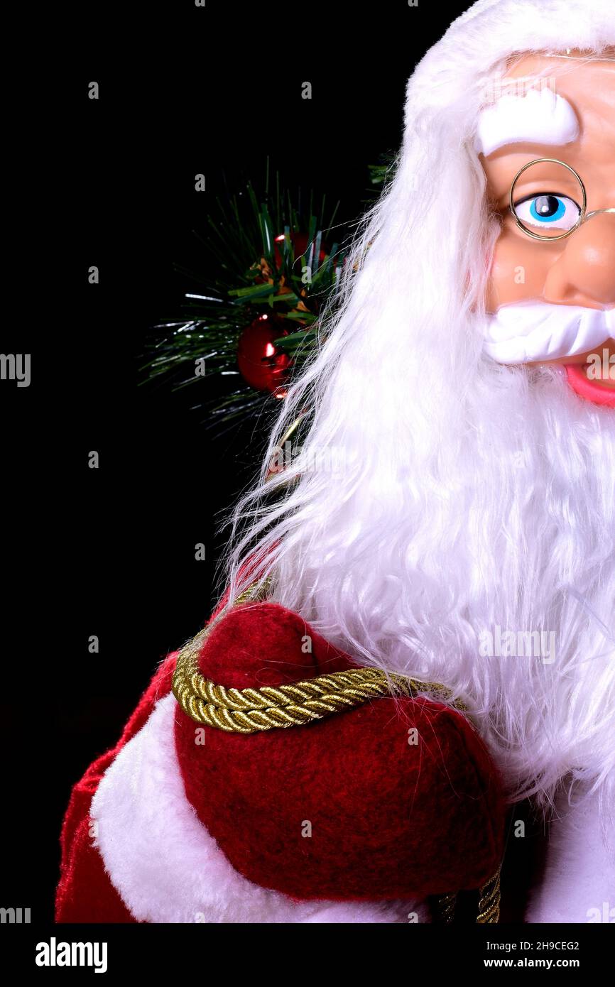 Photograph of a Santa Claus doll with his huge white beard and red suit.The photo is taken in the studio on a black background and in vertical format. Stock Photo