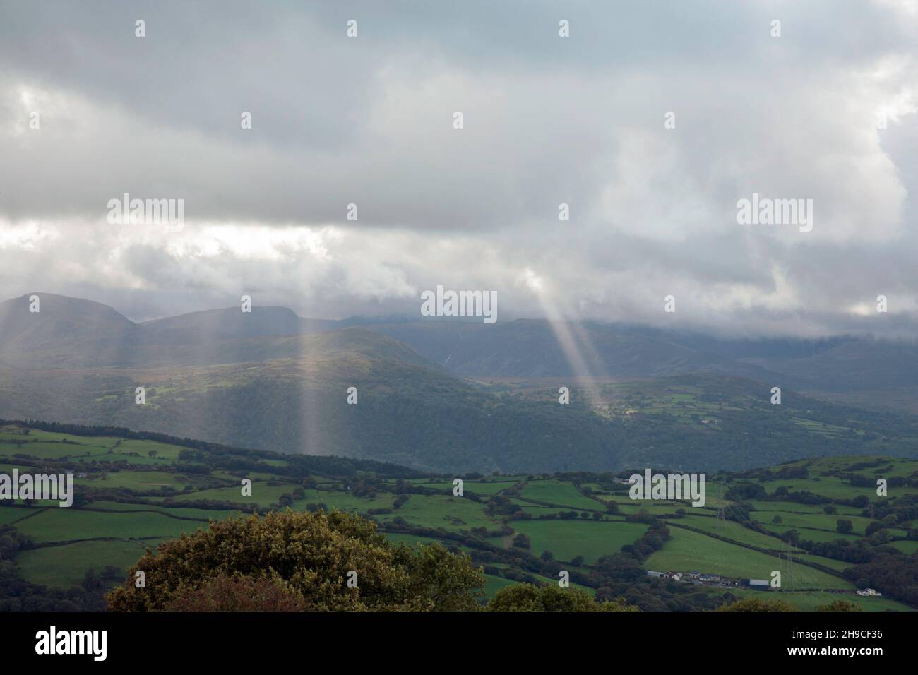 Storm clouds and shafts of sunlight passing across the mountains of the Conwy Valley from near the village of Eglwysbach Conwy Snowdonia North Wales Stock Photo