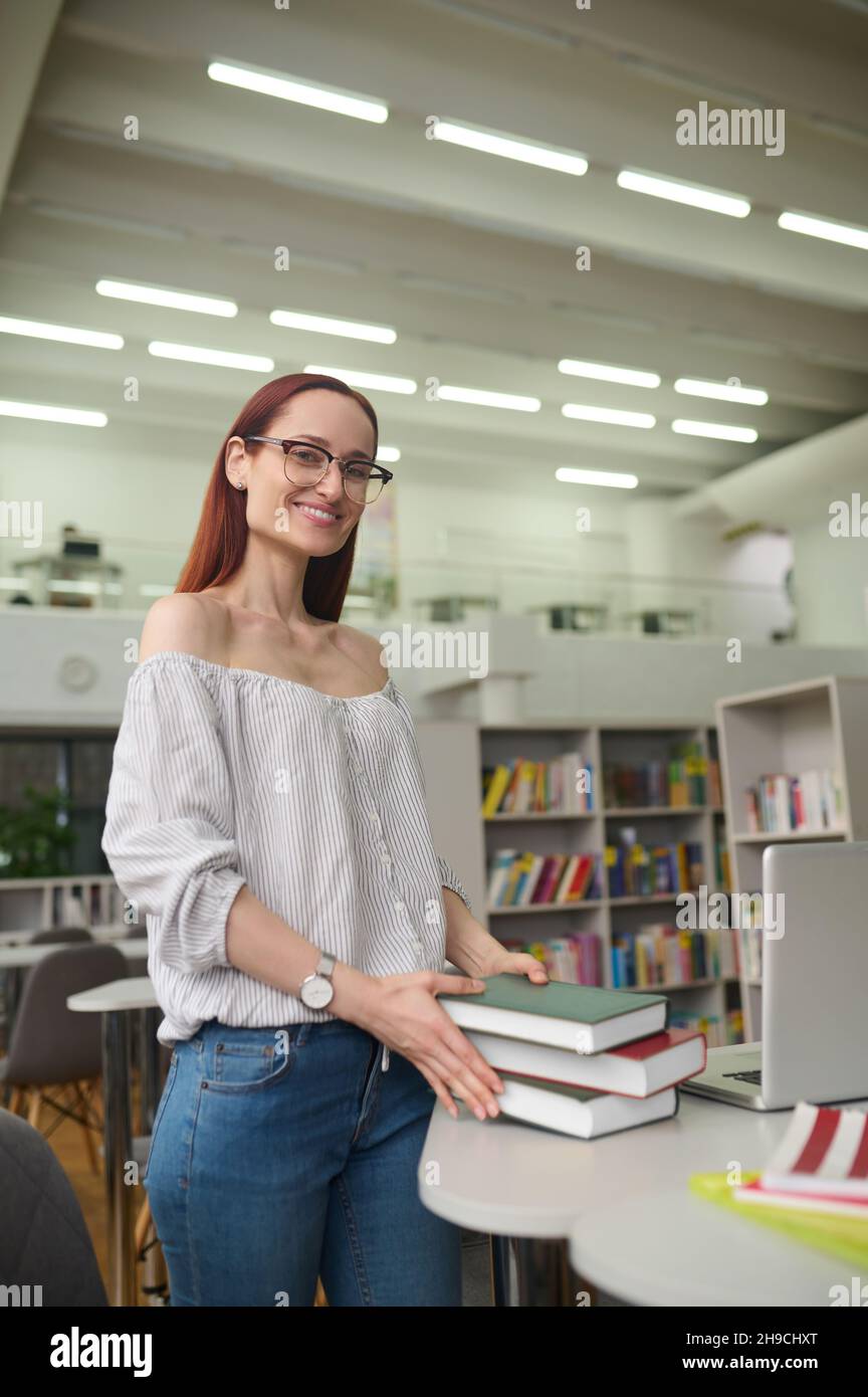 Woman with stack of books standing near table Stock Photo