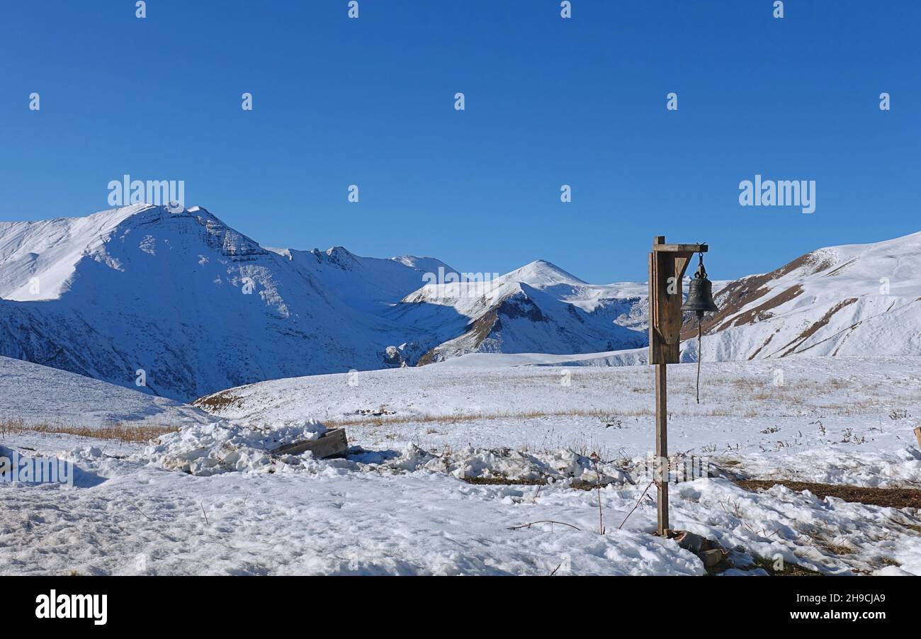 Bell in the middle of snowy mountains - trekking in Caucasus Stock Photo