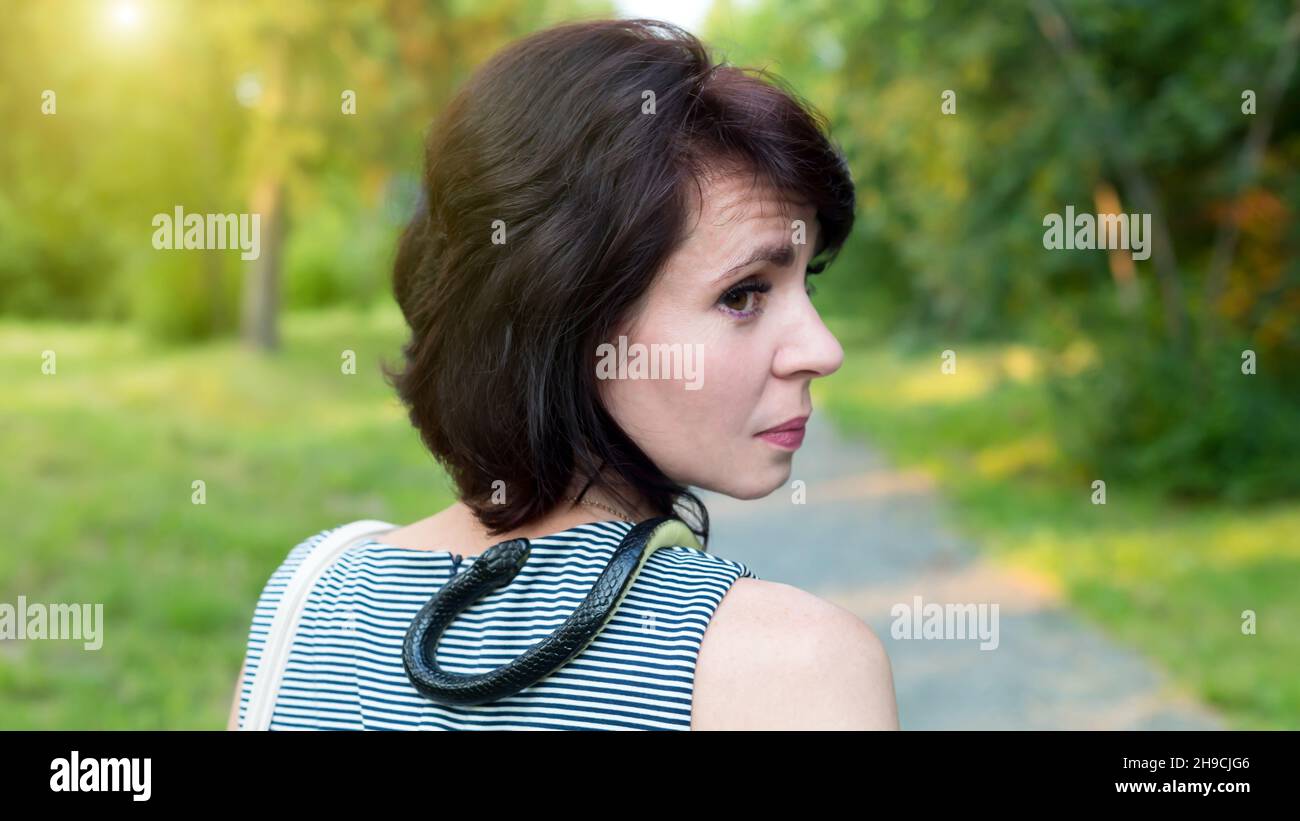 woman with live snake around her neck walks through the park. Stock Photo
