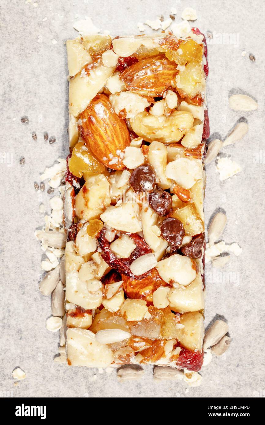 Natural granola cereal bar with nuts, seeds, oats, raisins and honey on a white pergament paper. Protein muesli bar. Granola superfood. Natural energy Stock Photo