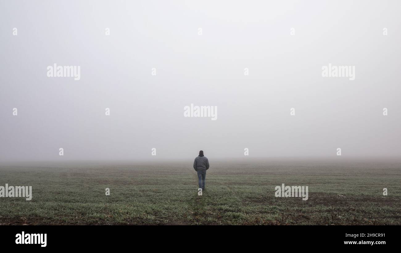 Lonly man  walk away into the misty foggy road in a dramatic mystic scene. Guy walking in a foggy autumn landscape Stock Photo