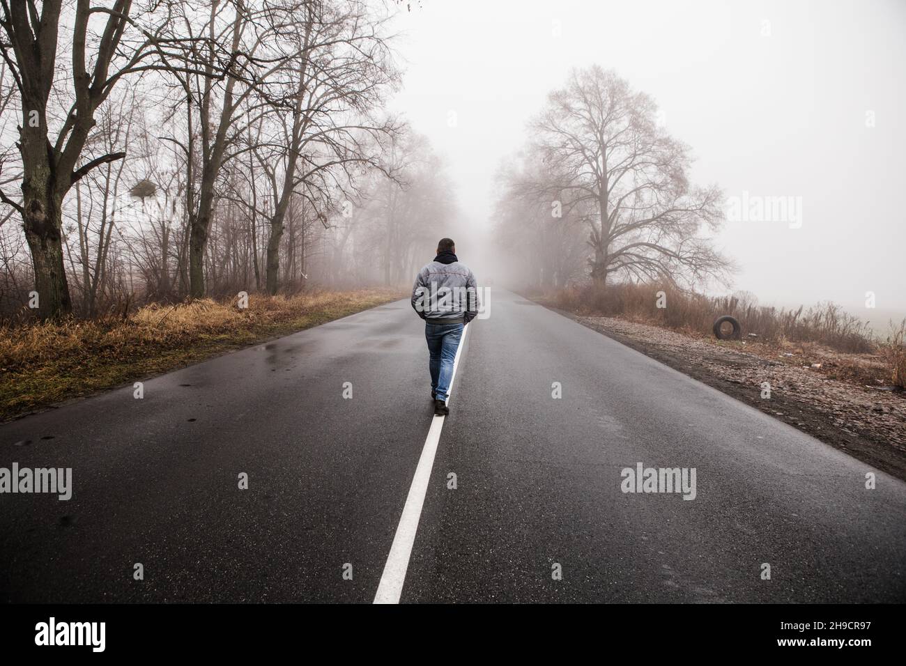 Lonly man  walk away into the misty foggy road in a dramatic mystic scene. Guy walking in a foggy autumn landscape Stock Photo