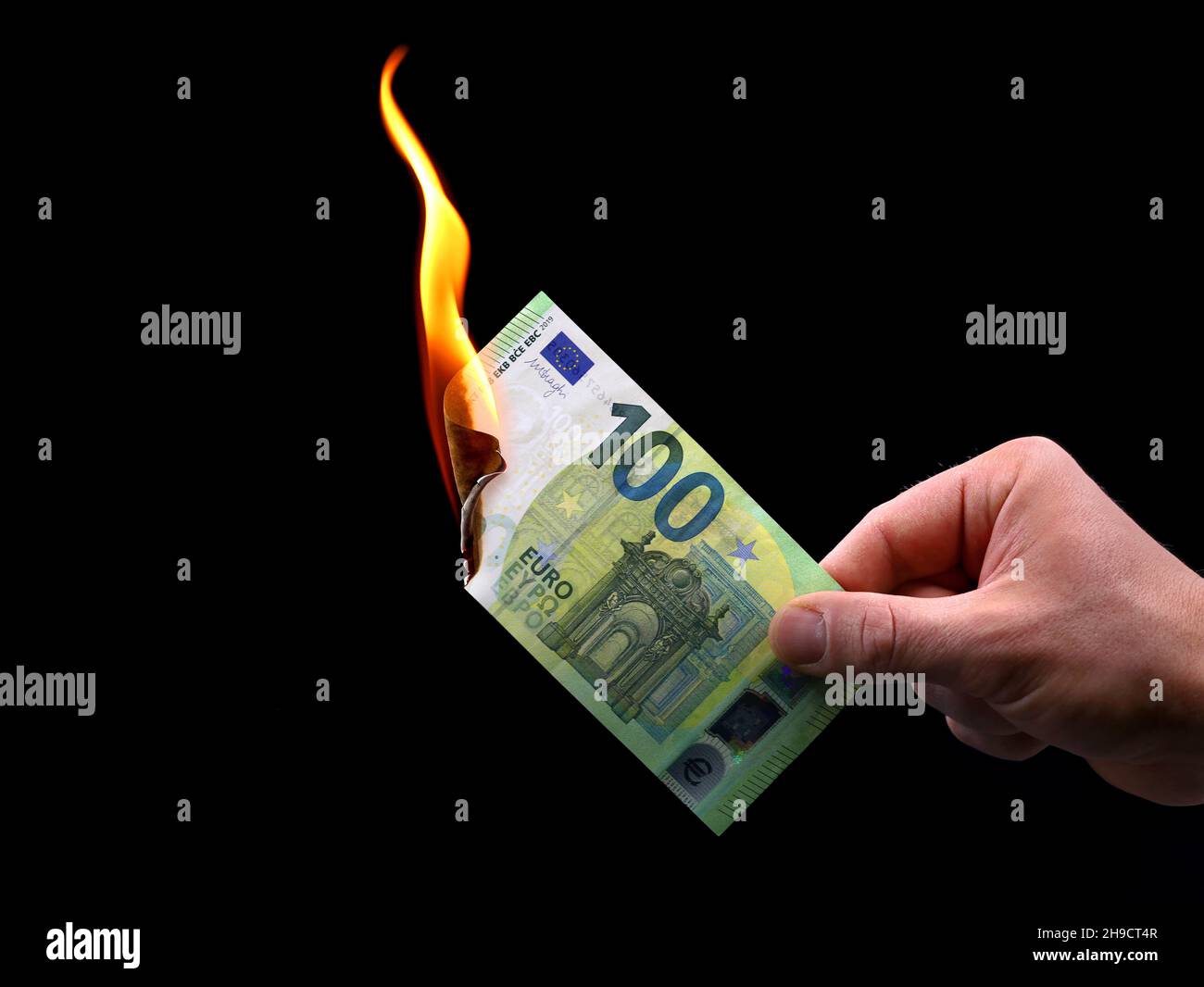 male hand holds a burning 100 euro banknote isolated on black background, concept image of inflation Stock Photo