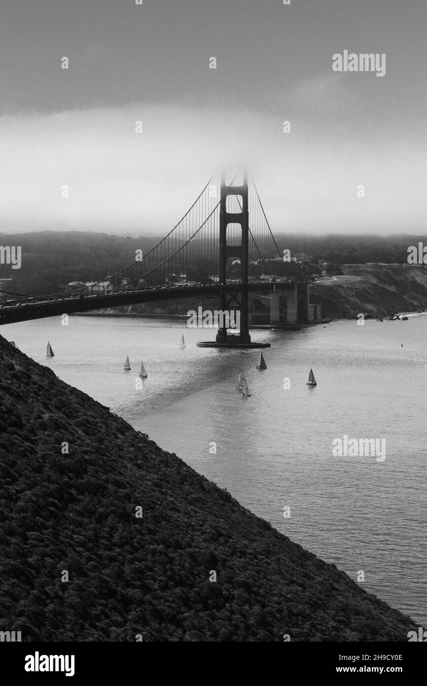 Vertical grayscale shot of the golden gates bridge under a misty sky in ...