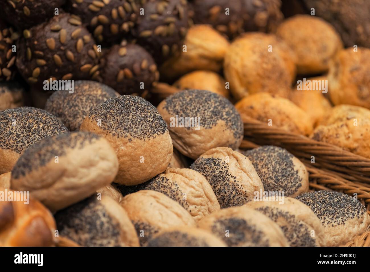 Close-up photo of breakfast lines of  rye buns with sunflower seeds and white wheat buns with poppy seeds in wooden trays at the hotel restaurant. Stock Photo
