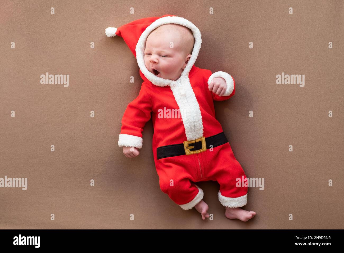 Newborn girl dressed in santa claus costume yawning being tired. Stock Photo