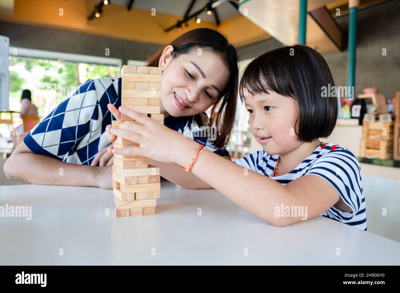 Little girl kid and mother playing Jenga wooden blocks game. Having fun and learning creativity ,selected focus on child eye Stock Photo