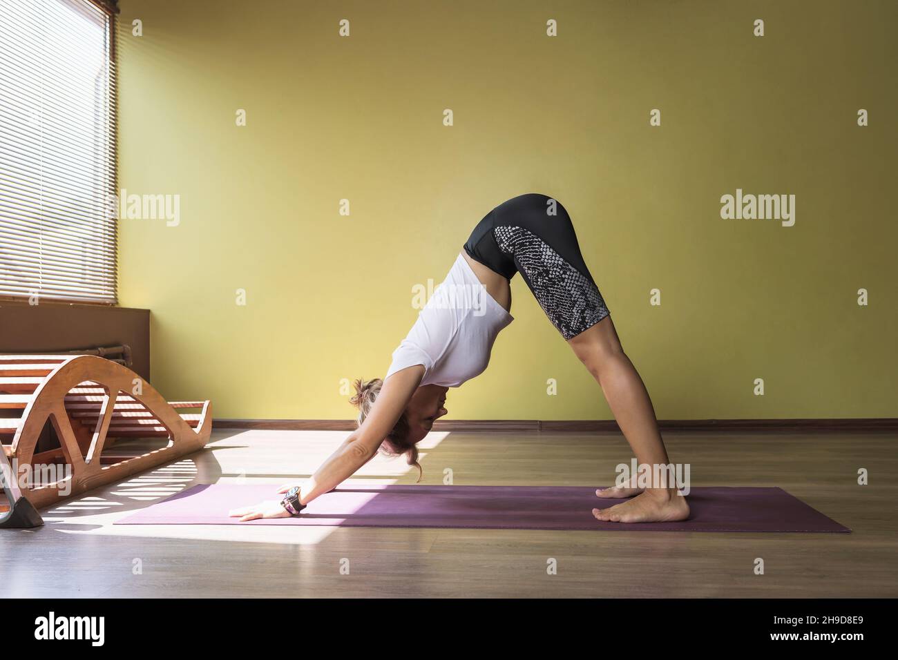 A woman performs the exercise Adho Mukha Svanasana, dog face down pose, exercising in sportswear on a mat in the studio Stock Photo