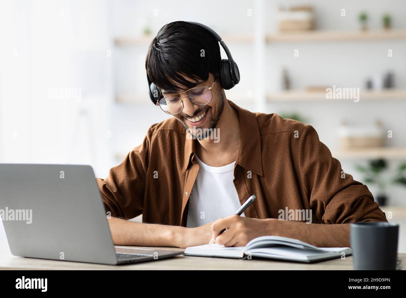 Joyful middle eastern guy attending webinar, using laptop, taking notes Stock Photo