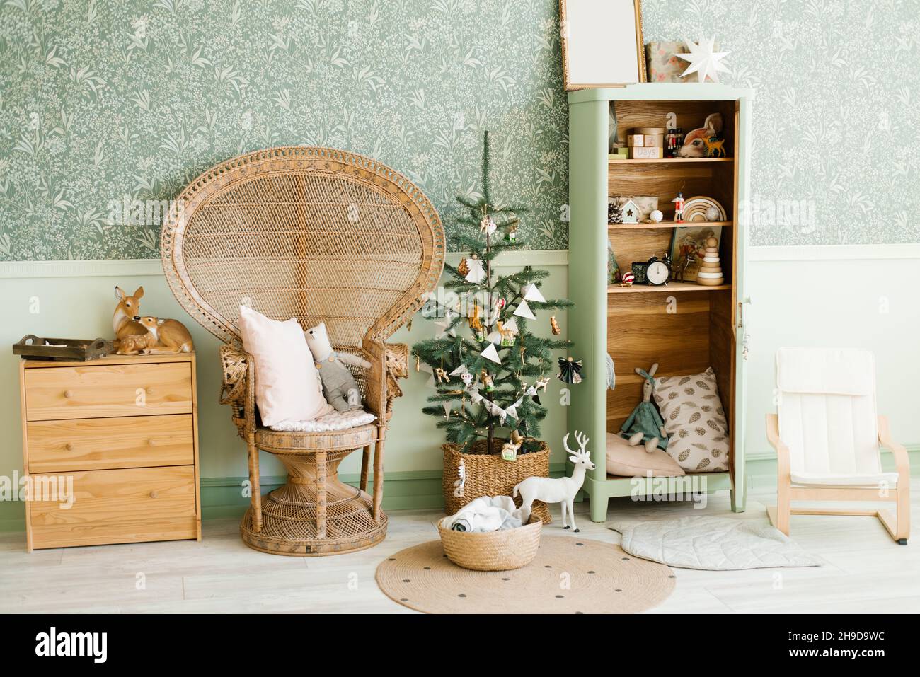 New Year's decor of the children's room: a wicker armchair with pillows, a Christmas tree with toys, a wardrobe and a chest of drawers in vintage styl Stock Photo