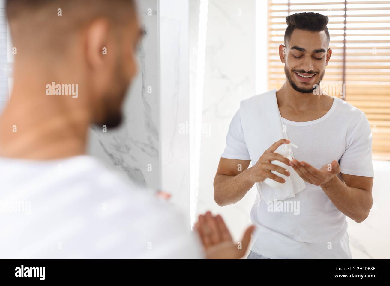 Men Skincare. Handsome Young Arab Man Using Aftershave Lotion In Bathroom Stock Photo