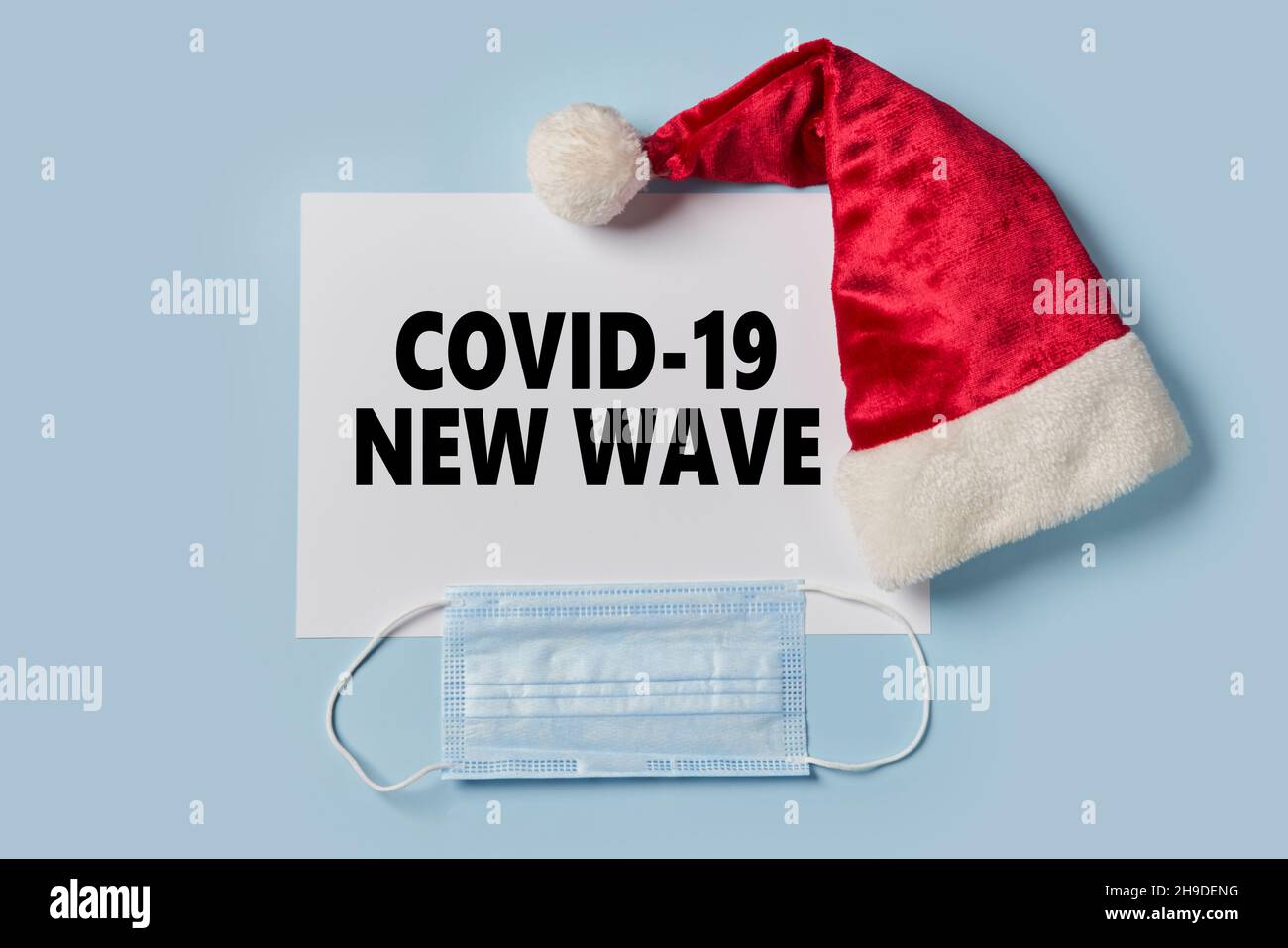 Covid-19 new wave during Christmas holidays. Santa Claus cap and surgical face mask. Coronavirus new wave text on paper and face mask. Lockdown Stock Photo
