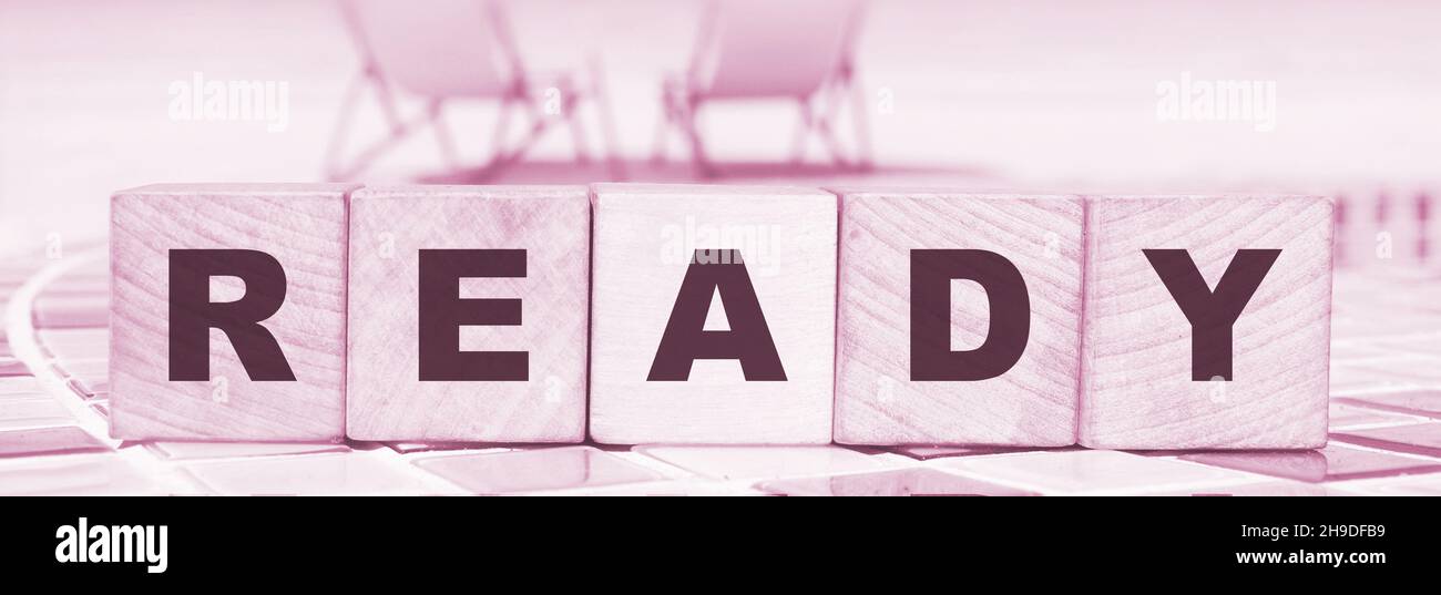 word ready made with wooden blocks standing on swimming pool border ...
