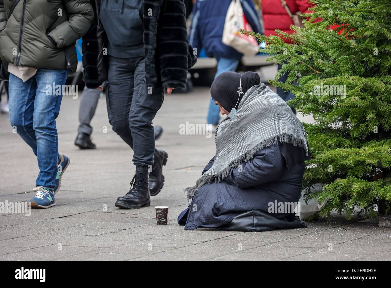 Essen, North Rhine-Westphalia, Germany - Beggar woman sits on the pavement in the pedestrian zone during the Corona pandemic at Christmas time. Passer Stock Photo