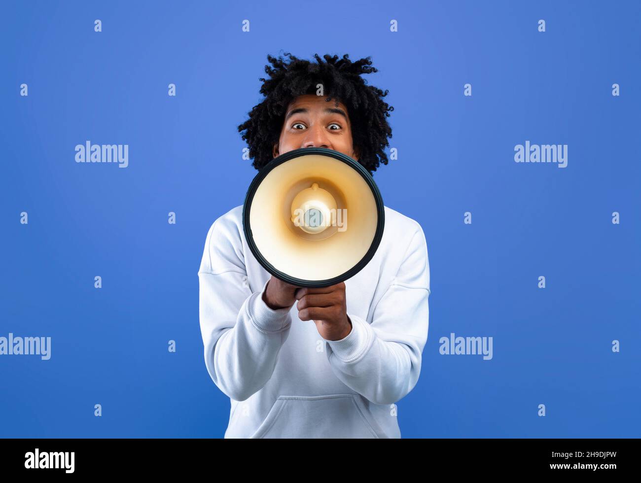 Emotional black teenager making announcement with megaphone on blue studio background Stock Photo