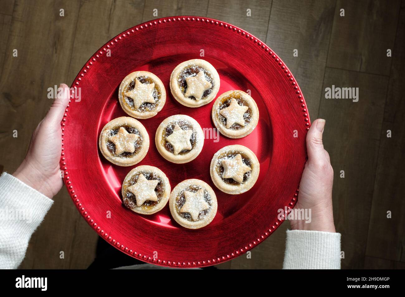 A woman holding a red festive plate thats filled with home made mince pies. Each pie has a traditional mincemeat filling  is topped with a pastry star Stock Photo