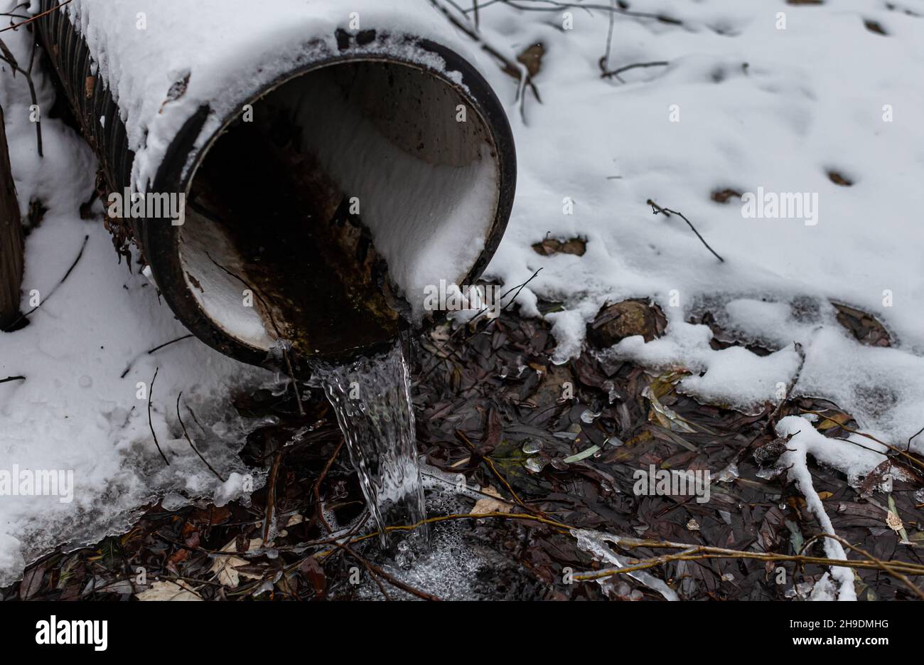 an iron snow-covered pipe from which a stream of water flows Stock Photo