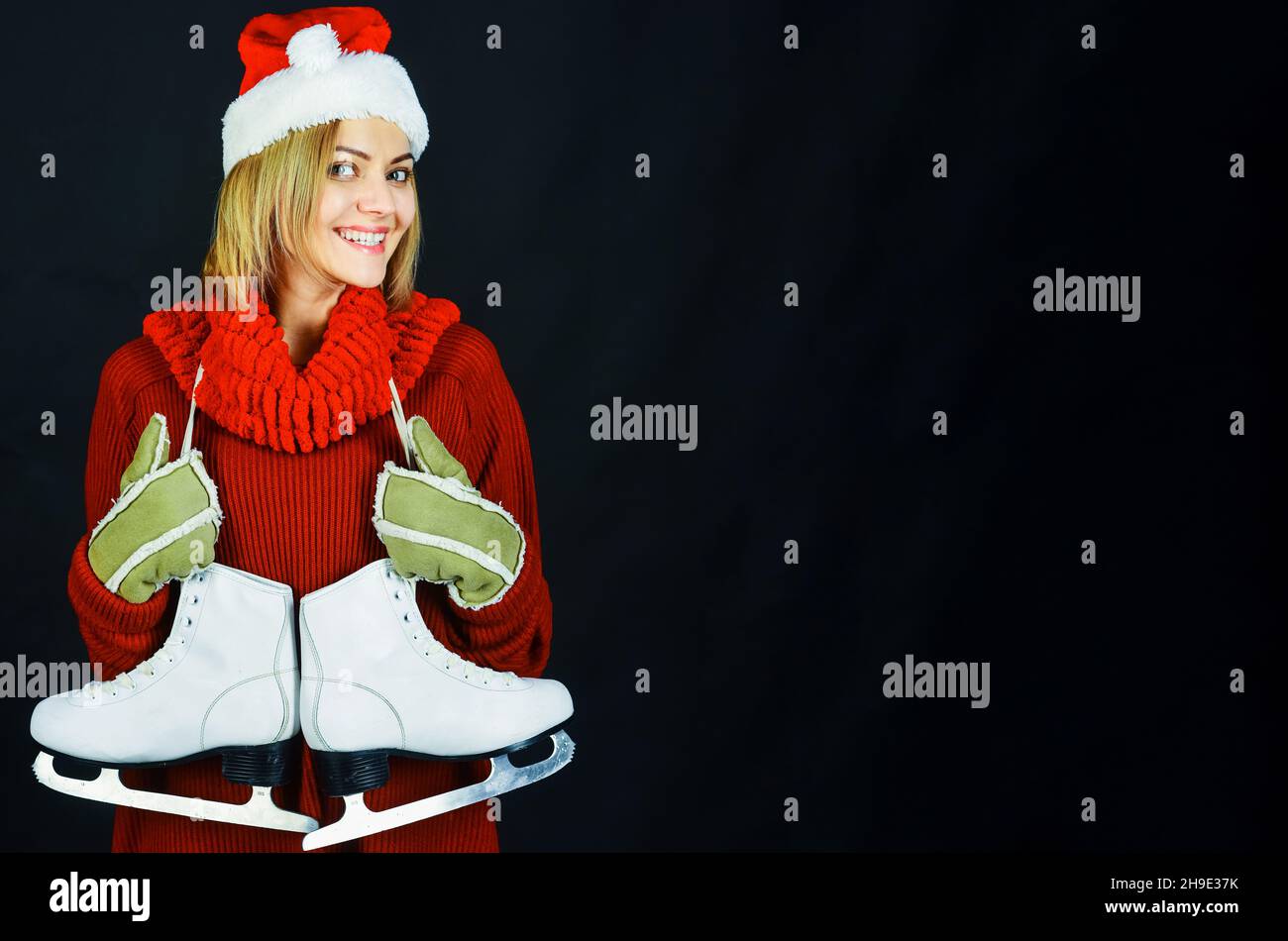 Ice skating. Happy woman in Santa hat, scarf and warm sweater with ice skates. Winter sport and leisure. Copy space. Stock Photo