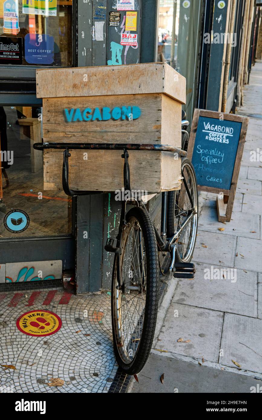 Traditional delivery bicycle with wooden box carrier with Vagabond painted on front parked outside Vagabond 7 Cafe Holloway Road Islington London Stock Photo