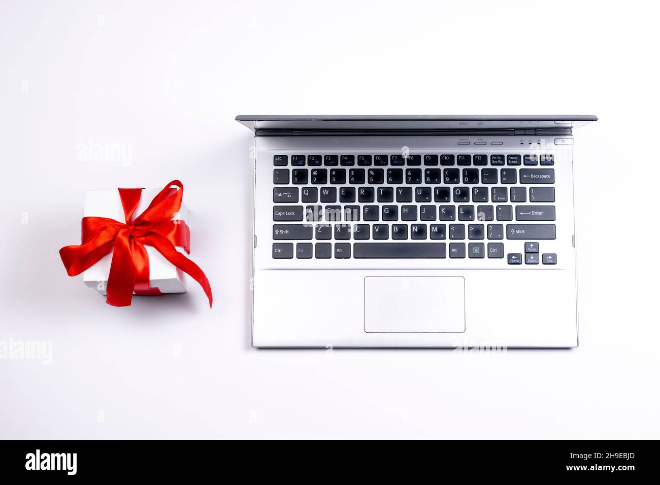 Old laptop and gift box with red ribbon on white background. Used silver notebook and present. Stock Photo