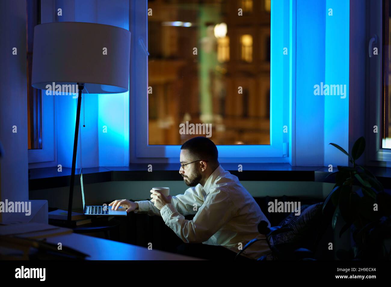 Tired web designer spend night at work before project launch working on laptop and drinking coffee Stock Photo