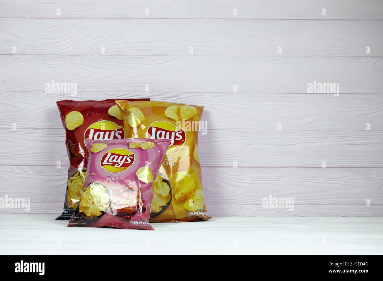 KHARKOV, UKRAINE - JANUARY 3, 2021: Various flavoured of lay's potato chips on wooden background. Lay's has been owned by PepsiCo through Frito-Lay si Stock Photo