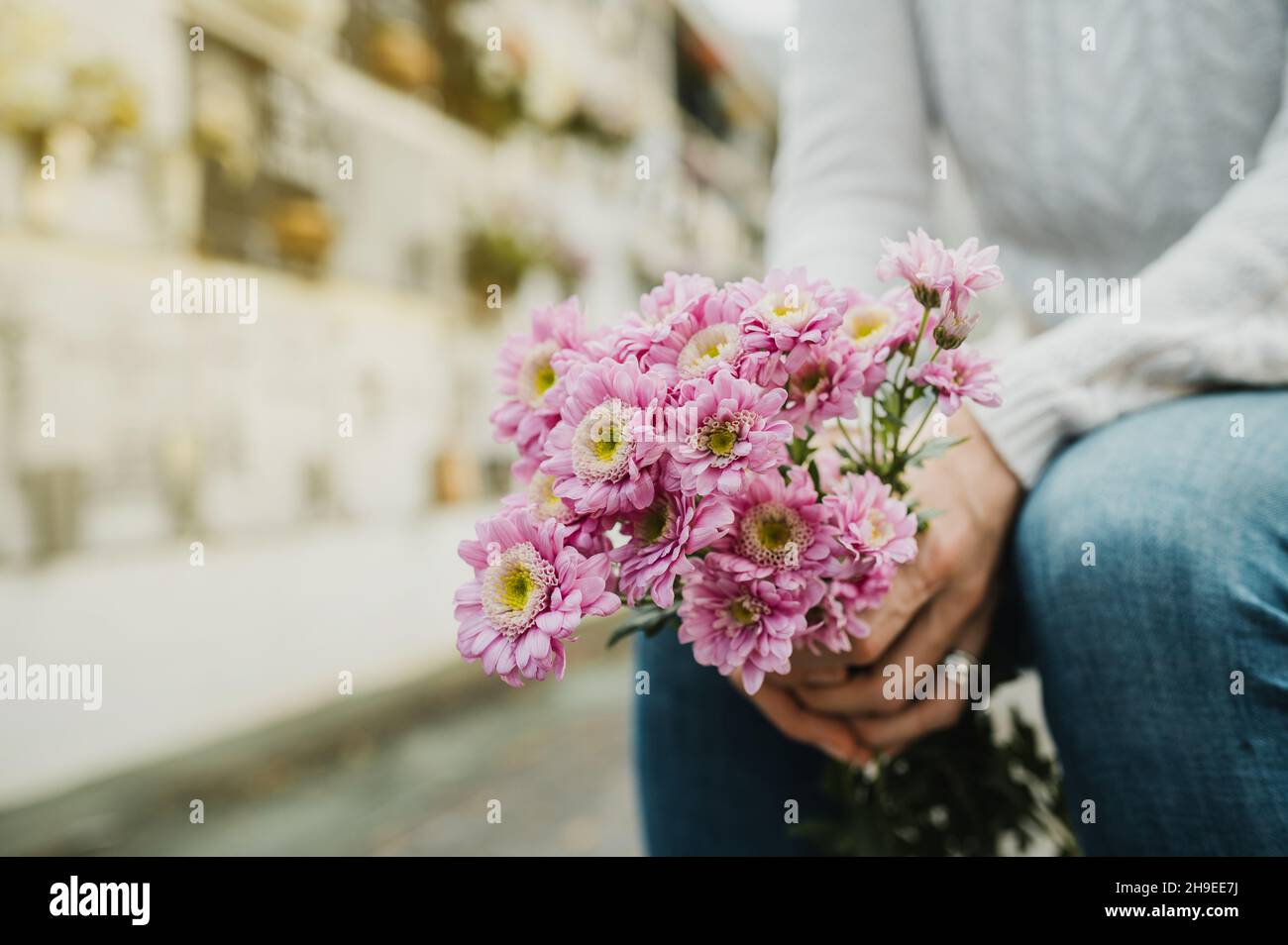 Faceless woman with flowers bouquet in hands sitting in cemetery Stock Photo
