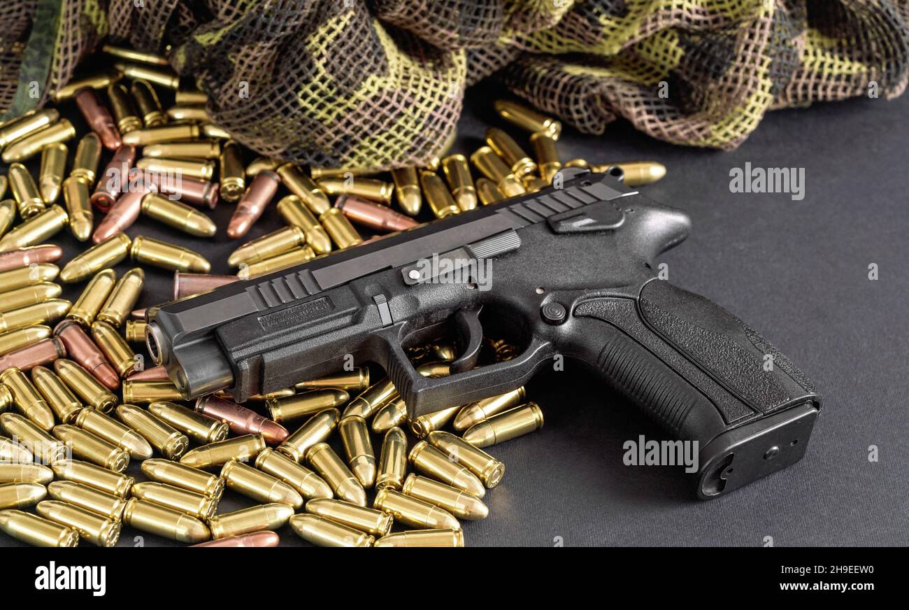 Yellow brass and brown bronze bullets, with black gun near, closeup detail Stock Photo