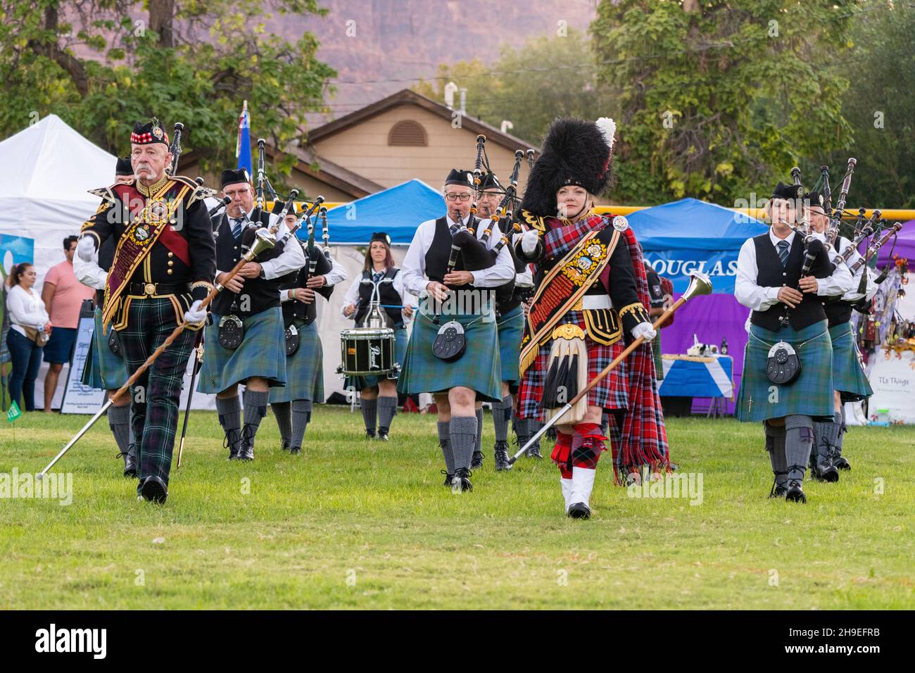 Male and female Highland band drum majors in full regalia lead a pipe band at a Scottish