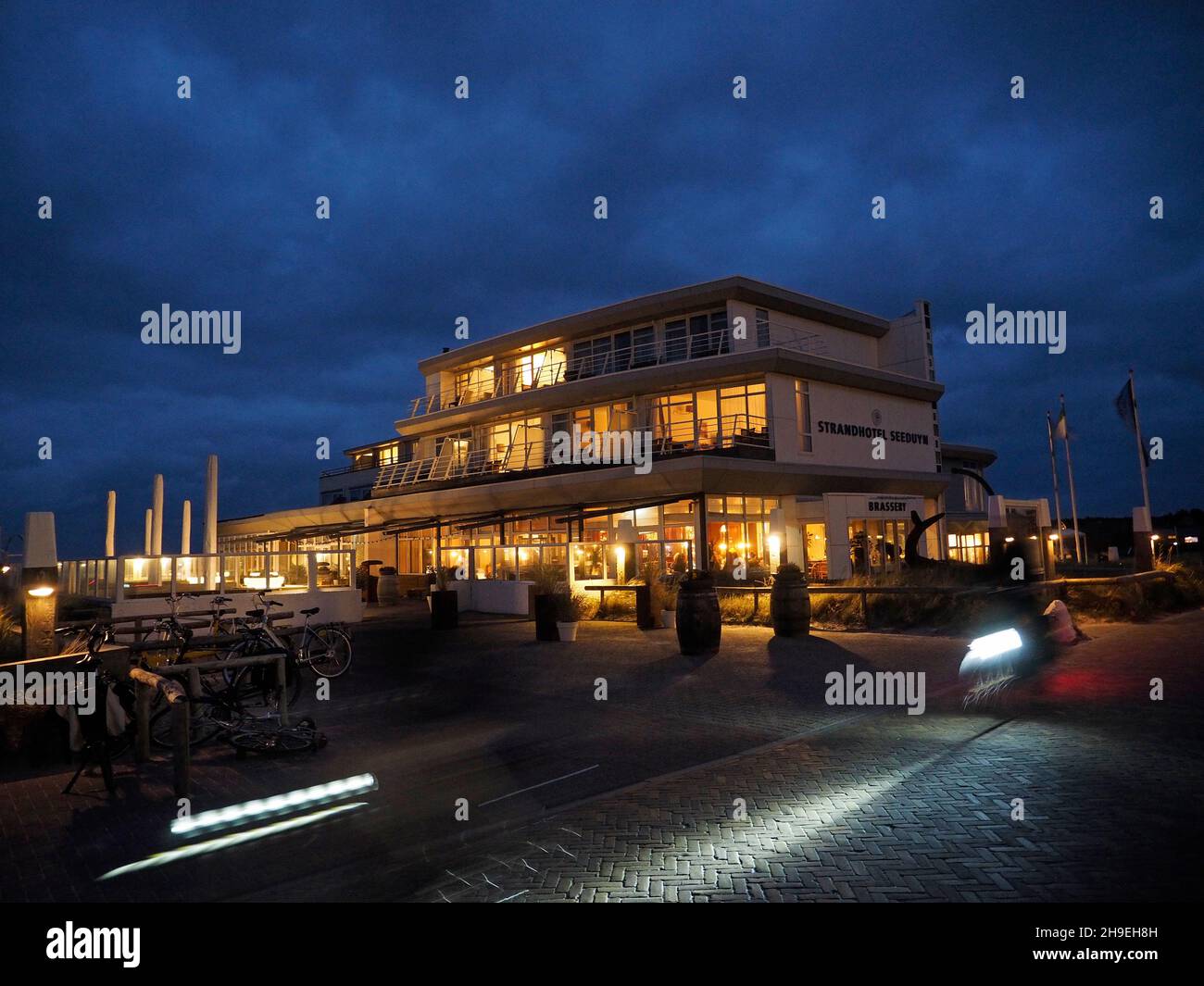 Evening shot of  Strandhotel Seeduyn with passing bicyclists, on Vlieland Island, Friesland, the Netherlands. The island is not car-free but tourists Stock Photo