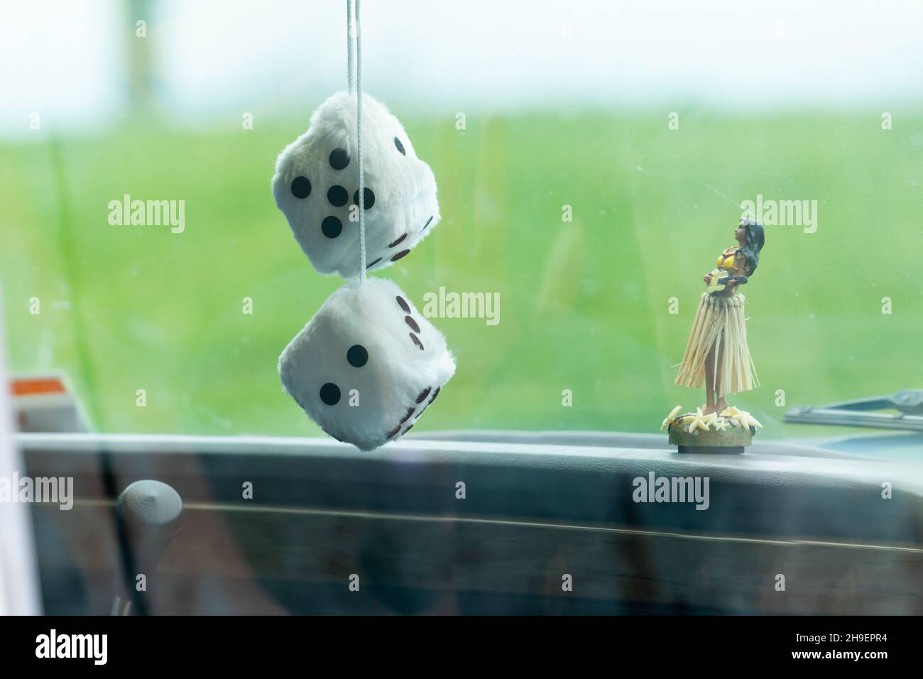 A pair of fuzzy dice hanging from a car's rear-view mirror beside a small dancing native lady on dashboard. Stock Photo