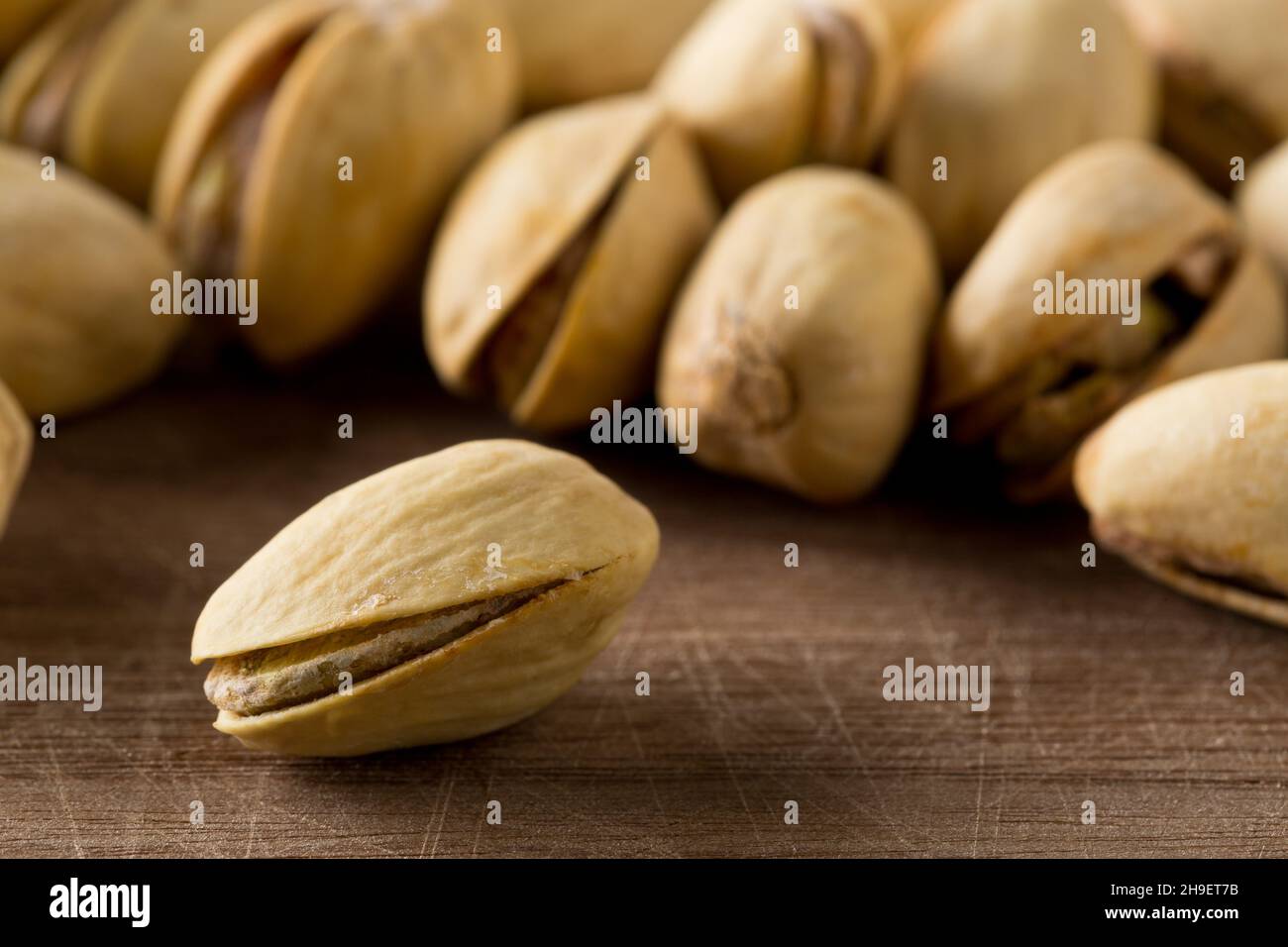 Close up of single pistachio in front of heap of salted, roasted green pistachio nuts snack over wooden background, healthy food snack, selective focu Stock Photo