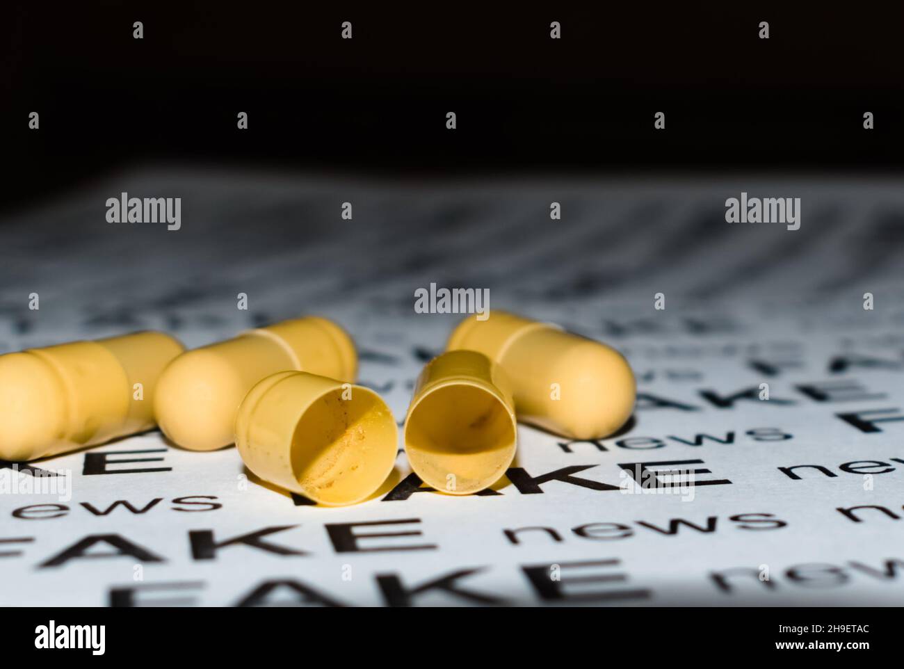 Empty opened medicine capsules on sheet of paper with text - FAKE news - on blurred dark background Stock Photo