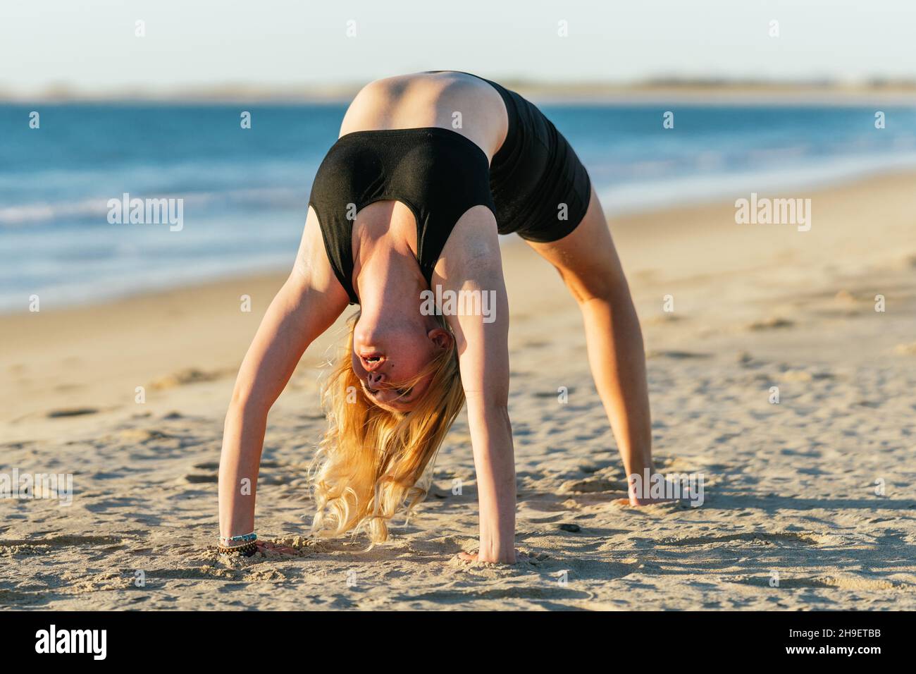Athletic blonde woman doing the bridge position of yoga on a beach Stock Photo