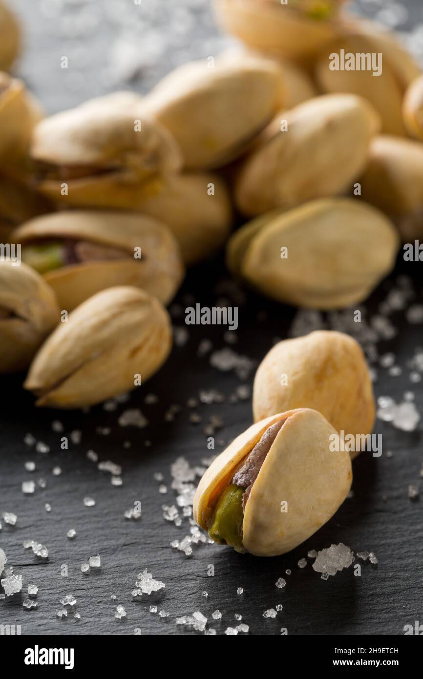 Macro of salted, roasted green pistachio nuts snack on black background with sea salt, healthy food snack, selective focus Stock Photo