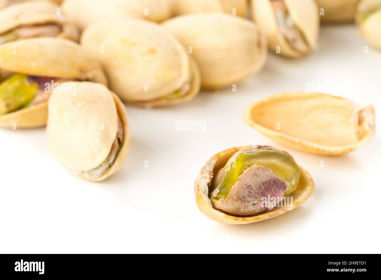 Close up of single, open pistachio in front of heap of salted, roasted green pistachio nuts snack over white background, healthy food snack, selective Stock Photo